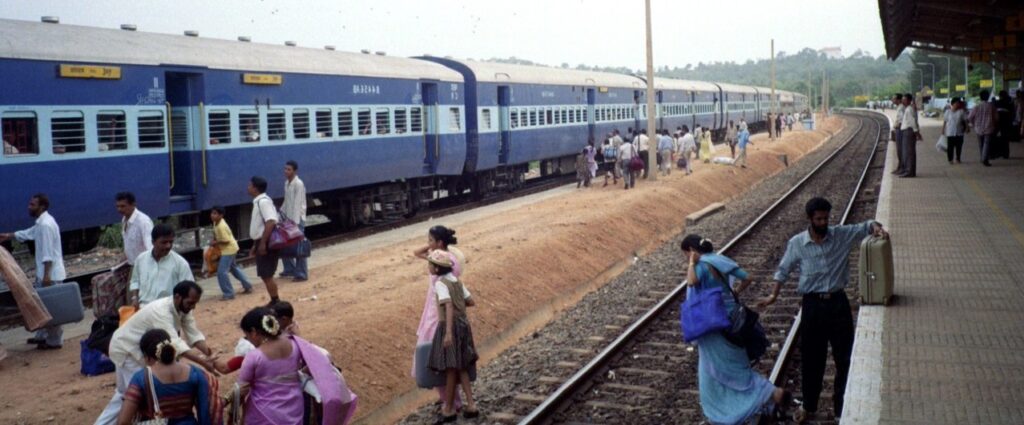 Indian Rail Journeys.   Passengers cross a rail track with luggage to climb aboard an Indian train.

