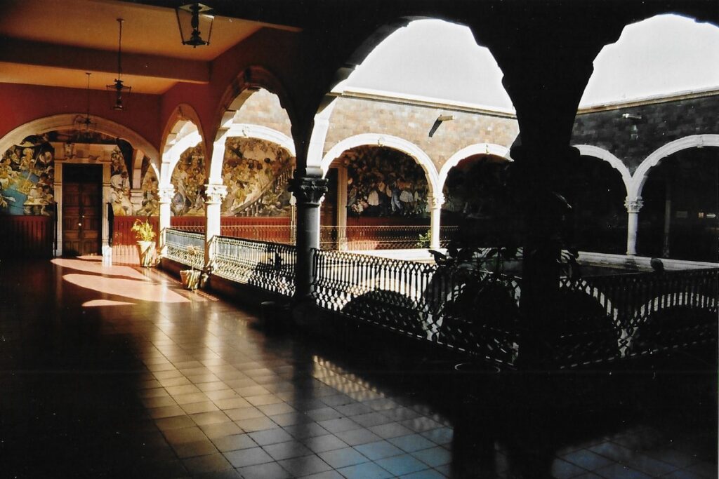 Mural strewn first floor walls of the municipal town hall, run around a balcony that look down onto a court yard.