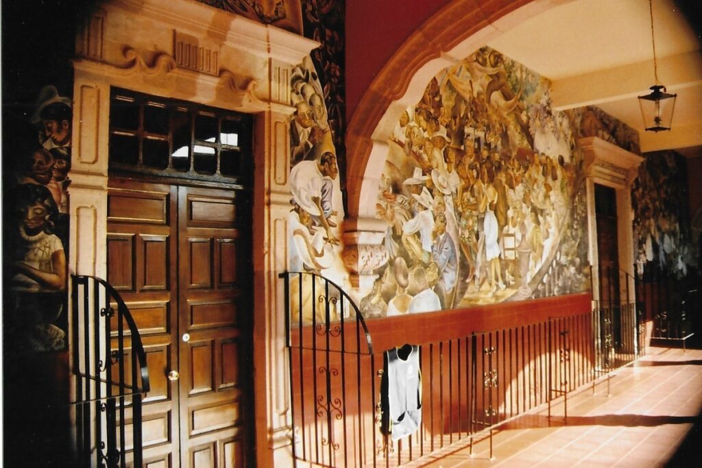 Mural strewn first floor walls of the municipal town hall, run around a balcony that look down onto a court yard.