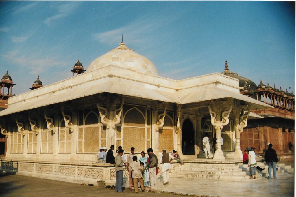 People chatting by the steps of a white staccato carved marble building, part of the ancient Mughal city of Fatehpur Sikri, India.
