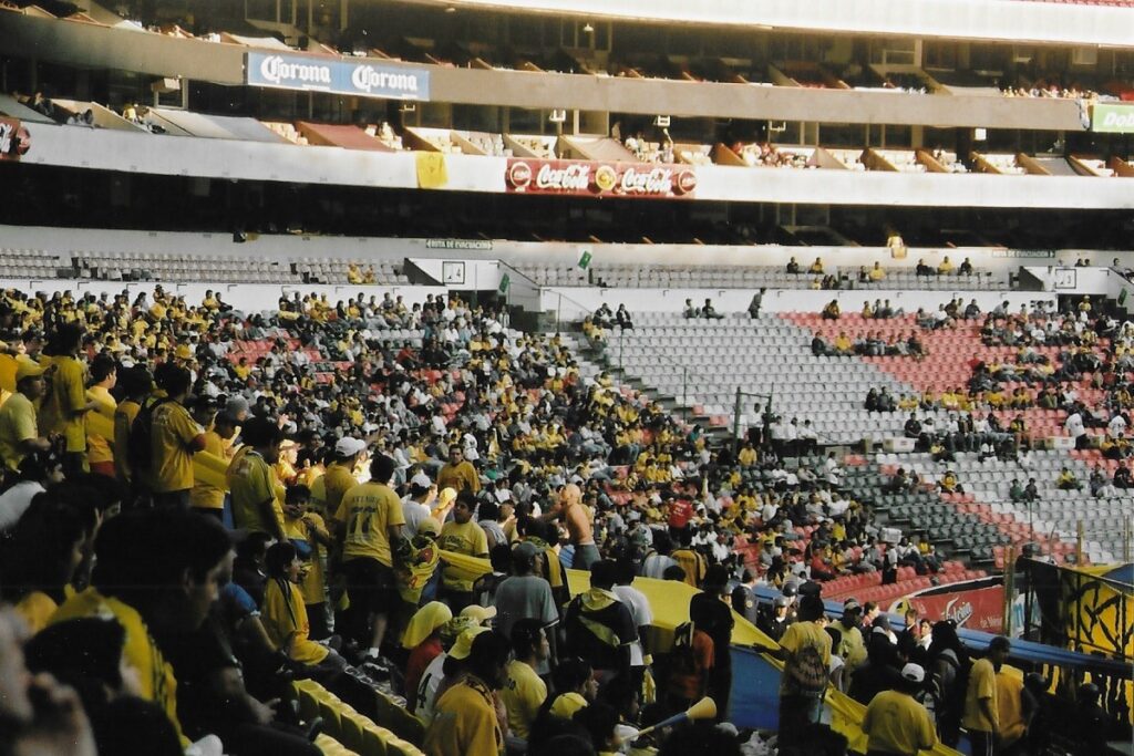 Crowd scene from inside the national Aztec Stadium in Mexico City during the course of a league game. Home team supporters in yellow shirts.