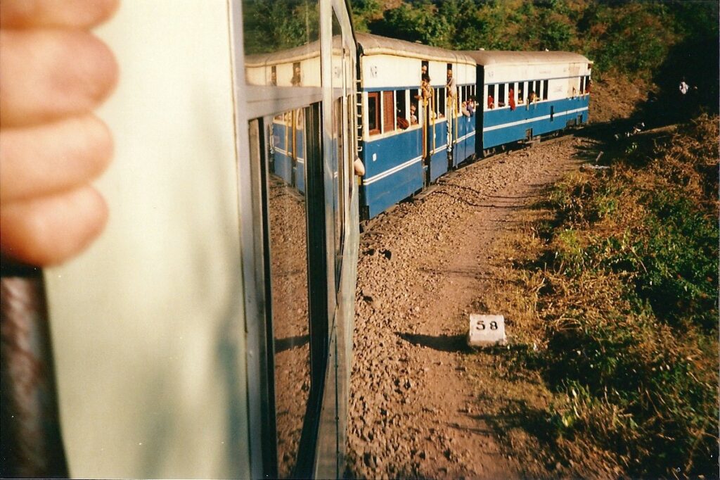 A view of the Simla to Kalka toy like train, as it rounds a bend. The author's hand visible as he holds on to one side of the doorway, leaning out to to take  the picture.
