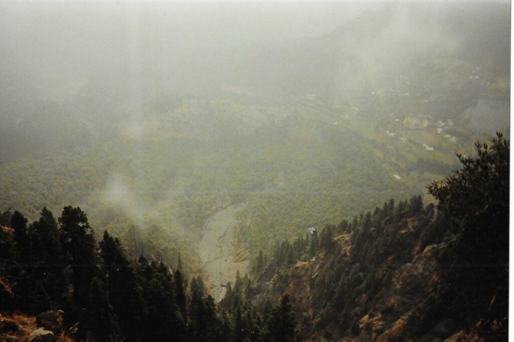 India travel writing. Above misty clouds, looking down from the Himalayan foothills high above Nainital through forest covered slopes.