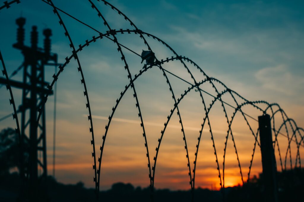 Iron Curtain Travels: silhouette of large barbed wire fence during sunset